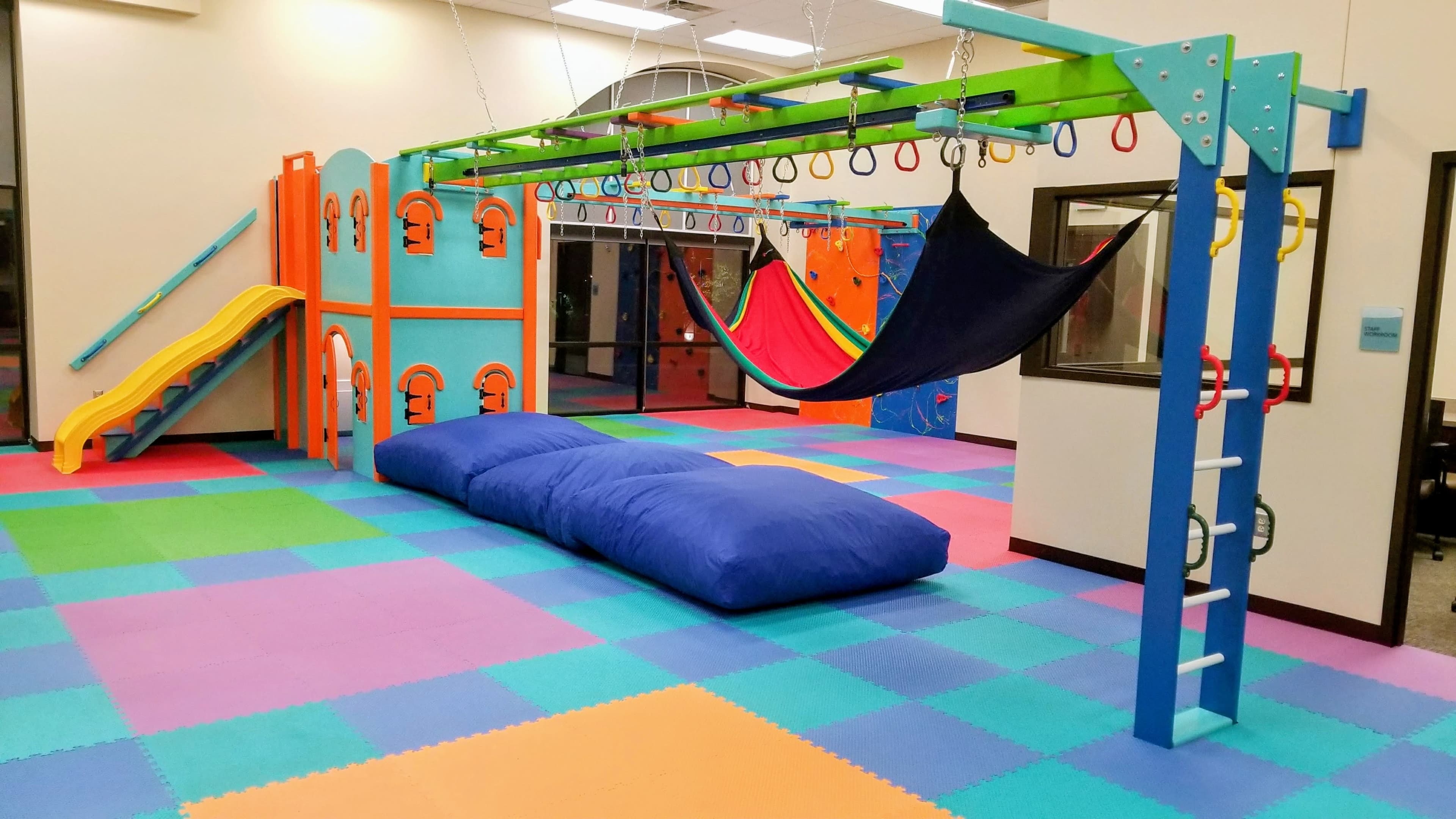 Commercial pediatric clinic sensory gym with climbing walls, slide, and hammock swing