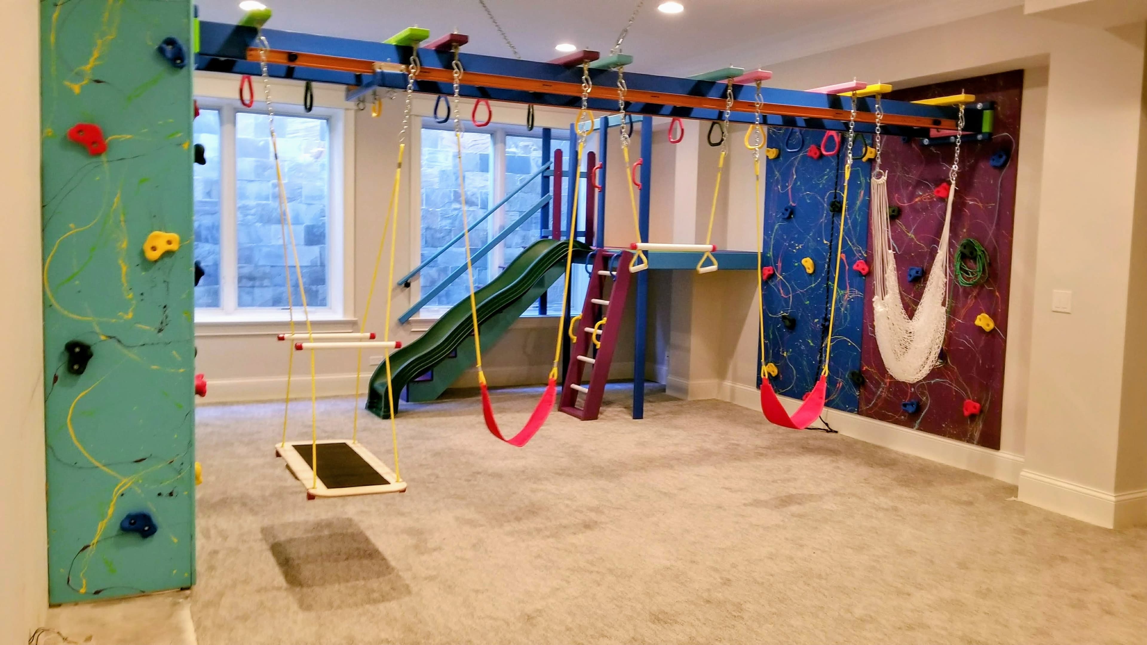 Carpeted basement sensory gym with splatter climbing walls, platform swing, hammock, and green slide